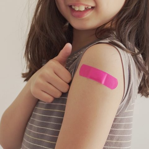 Child holding thumb up with pink bandaid